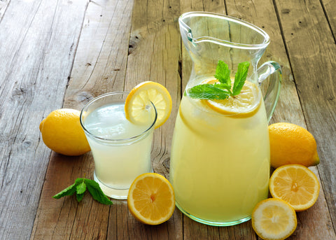Pitcher and glass of lemonade, garnished and decorated with fresh lemons and lemon slices